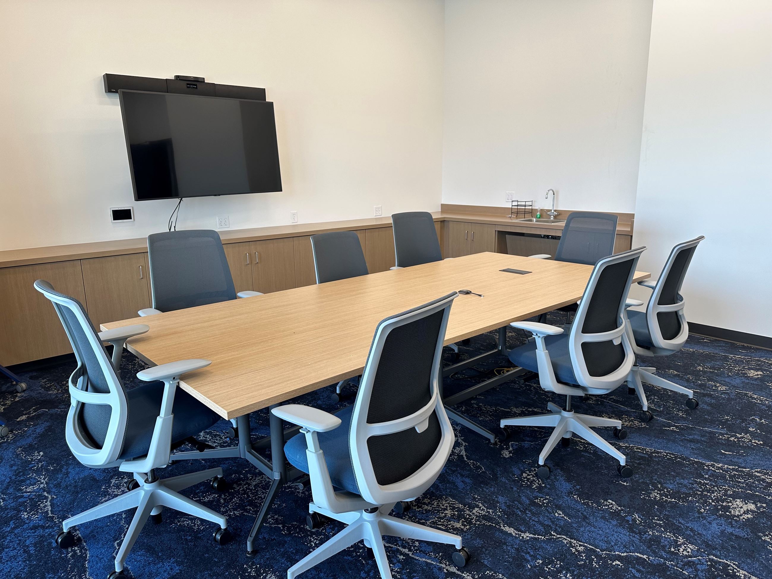 A room with table and 8 chairs with a TV on the wall 